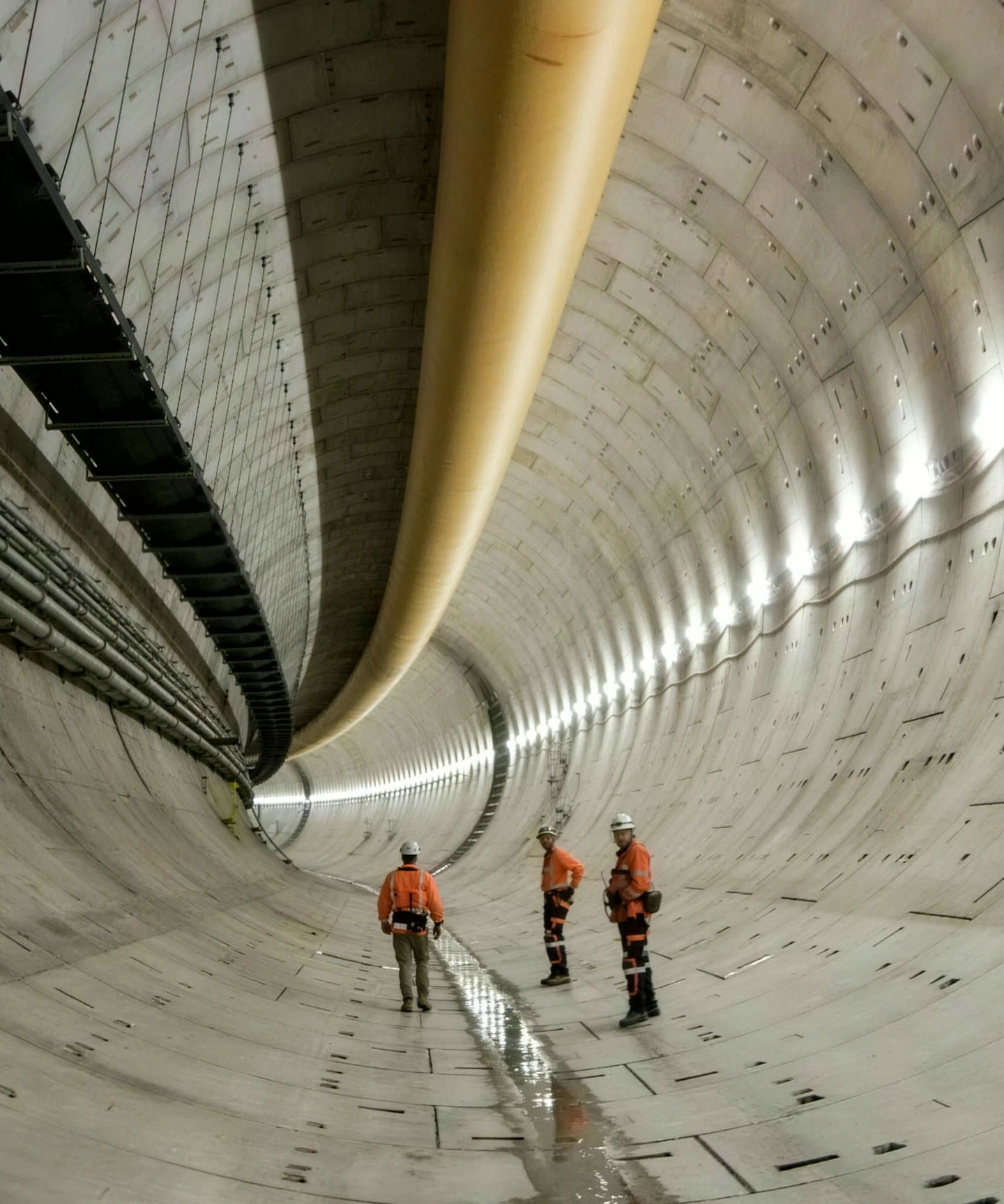 Three workers in orange high-visibility gear inside a segment-lined bored tunnel